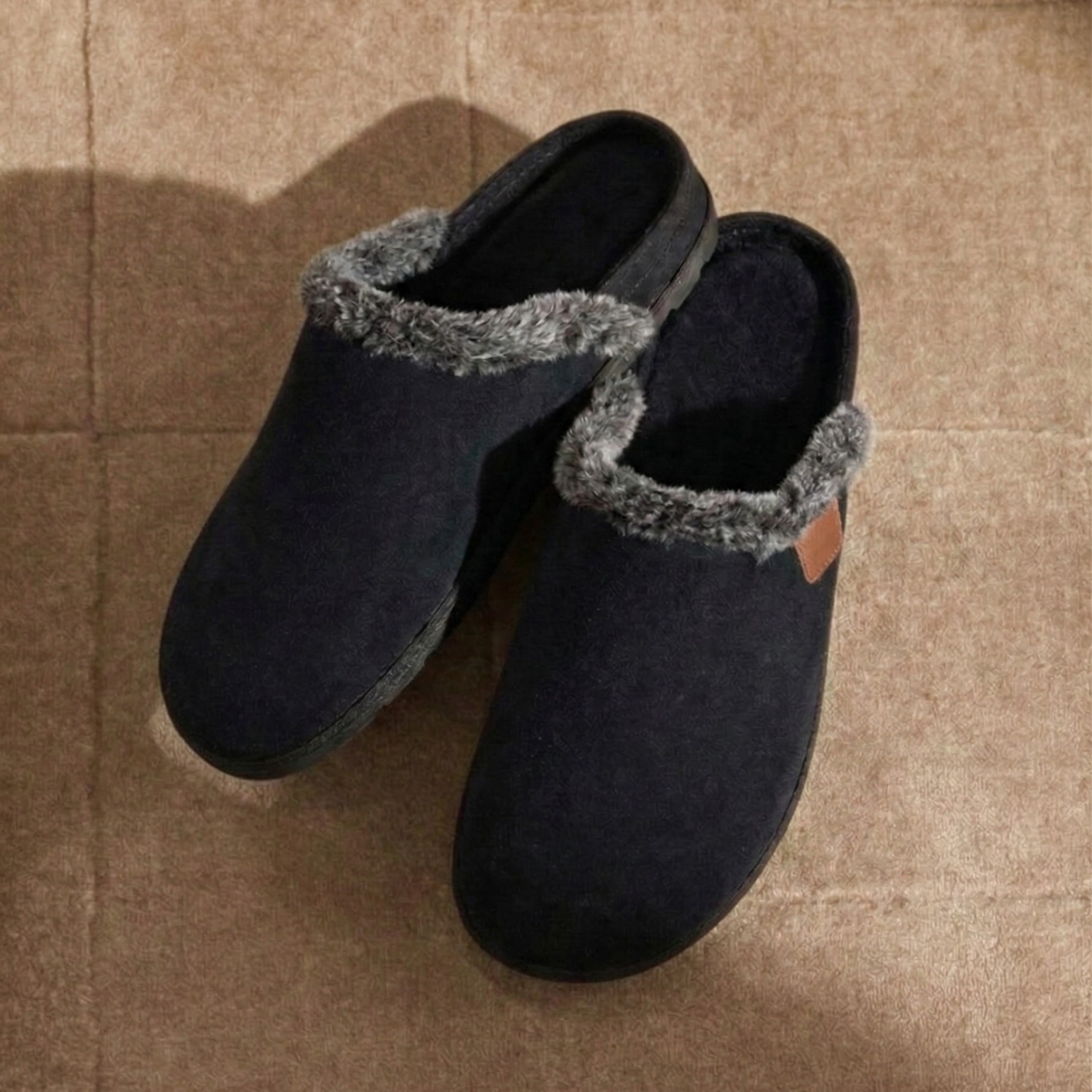 comfortable pair of black slippers with gray trim on a brown carpet. Soft cozy and warm